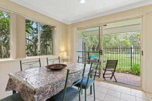a dining room with a table and chairs and a balcony at Treetops Lakeside Apartments in Byron Bay