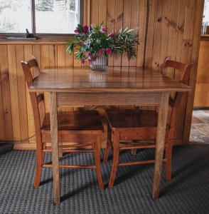 a wooden table with two chairs and a vase with flowers at Gaol House Cottages in Bicheno