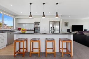 a kitchen with a large island with three bar stools at Campbell Road Classic - Mount Maunganui Bach in Mount Maunganui