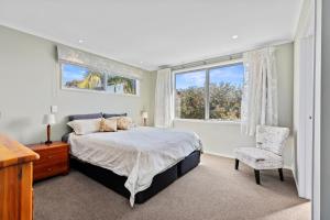a bedroom with a bed and a window and a chair at Campbell Road Classic - Mount Maunganui Bach in Mount Maunganui
