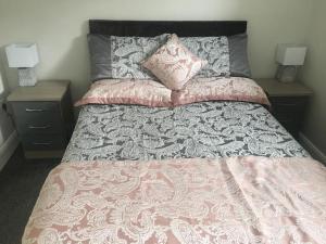 a bed with a pink and gray comforter and two night stands at Dympna's City Centre apartment, Armagh in Armagh