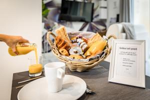 een tafel met een mand met eten en een persoon die sinaasappelsap schenkt bij Le Diamant - Appart'Hôtel SPA - Clim - Melina & Alfred Agen in Agen