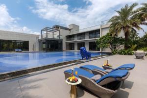 a house with a swimming pool with chairs and a blue statue at Colossus by StayVista - Riverside luxury villa in Khalapur with a Spacious pool, Sauna, Private theater, Gazebo & Lawn in Lonavala