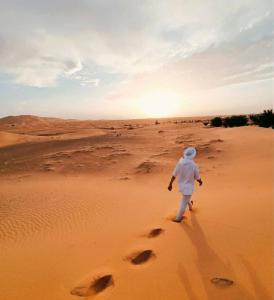Ein Mann, der durch die Wüste geht, mit der Sonne im Hintergrund in der Unterkunft Mhamid camp activités in Mhamid