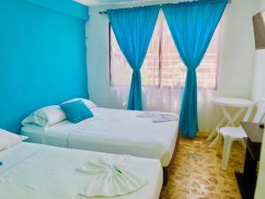 two beds in a room with blue walls and a window at Hotel Atuchi in Cartagena de Indias