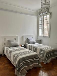 two beds in a room with white walls and a window at Departamento 6 personas Plaza San Martin in Buenos Aires