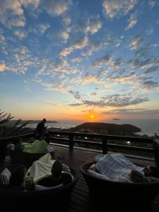 grupa ludzi siedzących na pokładzie obserwujących zachód słońca w obiekcie Pousada Mirante dos Papagaios w mieście Búzios