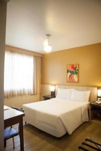 um quarto com uma grande cama branca e uma janela em Hotel Palmeiras em Laranjeiras do Sul