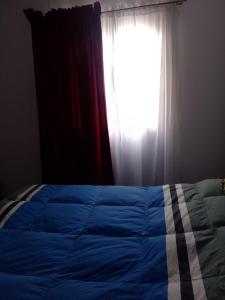 a bed with a blue comforter in front of a window at Ushuaia de las Nieves B&B in Ushuaia