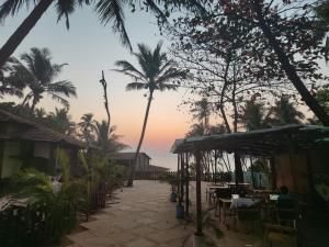 d'une terrasse avec des tables, des chaises et des palmiers. dans l'établissement Beachside, à Anjuna