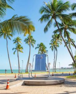 un banc bleu sur la plage avec des palmiers dans l'établissement Apartamento Beira Mar - Maceió, à Maceió