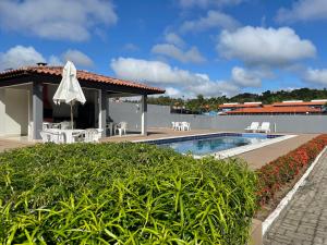 einem Pool mit Stühlen und einem Sonnenschirm neben einem Gebäude in der Unterkunft Apartamento no Taperapuan Duplex in Porto Seguro