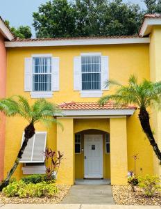 a yellow house with two palm trees in front of it at Enchanting Escape 3 Bedroom Minutes from Disney! in Kissimmee