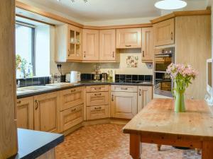 uma cozinha com armários de madeira e uma mesa com flores em The Moorings em Lochmaben