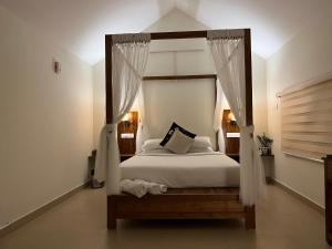 - une chambre dotée d'un lit à baldaquin avec des draps et des oreillers blancs dans l'établissement Titha Service Villa, à Santhanpara