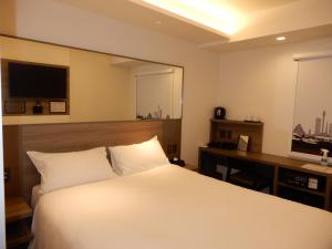 a bedroom with a bed and a desk with a television at Smile Hotel Hiroshima in Hiroshima