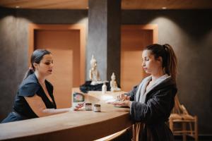 dos mujeres de pie en un mostrador hablando entre sí en Hotel Cristallo - Wellness Mountain Living, en La Villa