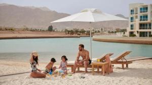 een gezin zittend op het strand onder een parasol bij Blue Diamond Ayla - Restricted to Family stays in Aqaba +10 foto's