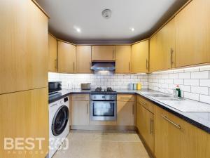 uma cozinha com armários de madeira e uma máquina de lavar e secar roupa em Redhill town centre apartment by Livingo em Redhill