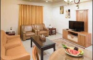 AL MANAF HOTEL SUITES في مسقط: غرفة معيشة مع تلفزيون وطاولة مع صحن من الفاكهة