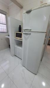 a white kitchen with a refrigerator and a microwave at SOL & MAR I com VARANDA - 1 dormitório - Canto do FORTE - 300 m da Praia e 20m da Avenida dos Barzinhos - ESTACIONAMENTO gratuito e WI Fi 300mbytes com TV a cabo - ap113 in Praia Grande