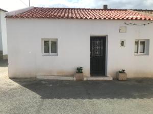 a white house with a black door and two plants at Casa das Flores - no Parque Natural Guadiana in Mértola