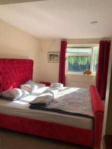 a bedroom with a bed with a red headboard and a window at Spacious Furnished Bungalow with Garden n Parking in Bradenham
