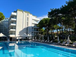 a swimming pool with lounge chairs and a building at Hotel Greif in Lignano Sabbiadoro