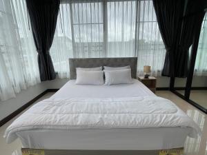 uma cama com lençóis brancos e almofadas num quarto com janelas em Service Apartment ใจกลางเมืองใกล้แหล่งท่องเที่ยว119ทับ1ถนนปงสนุก em Lampang