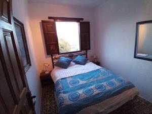 een slaapkamer met een bed met blauwe kussens en een raam bij Unique Village House in Jimena de la Frontera