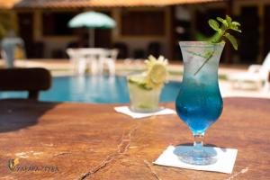 a blue drink in a glass on a table next to a pool at Pousada Yapara-Tyba in Japaratinga