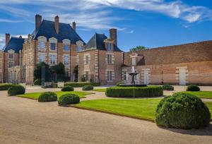 un grand bâtiment en briques avec une cour entourée de buissons dans l'établissement La Borde en Sologne Château & Spa, à Vernou-en-Sologne