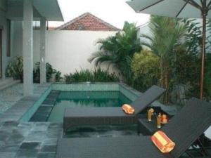 a swimming pool with two chairs and an umbrella at Villa Rob in Kerobokan