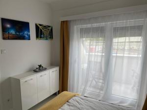 Schlafzimmer mit einem Bett und einem Fenster mit einem Stuhl in der Unterkunft Quelle-Apartman in Győr