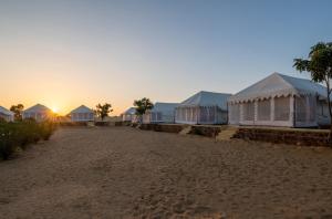 rząd namiotów na plaży z zachodem słońca w obiekcie Rajwada Desert Camp w mieście Jaisalmer