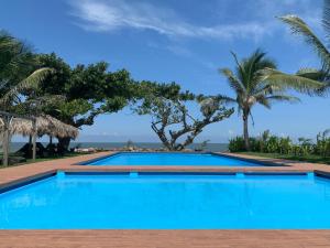 a blue swimming pool with palm trees and the ocean at Mar De Estrellas - Hotel in Costa Esmeralda