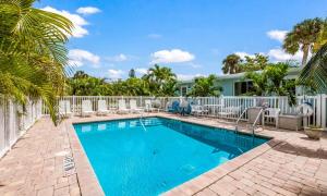 a pool with chairs and palm trees in front of a house at Driftwood Villas at Anna Maria Island Inn in Holmes Beach