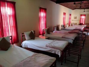 fila de camas en una habitación con cortinas rojas en Naurang Yatri Niwas en Garli