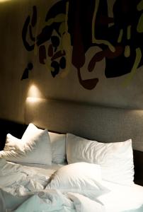 a bed with white pillows and a painting on the wall at ARTOTEL Haniman Ubud in Ubud