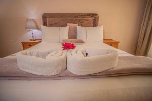 Una cama con toallas blancas y una flor roja. en Palm villa en Harare