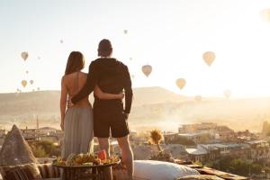 um homem e uma mulher de pé numa varanda a olhar para balões de ar quente em Doors Of Cappadocia Hotel em Goreme