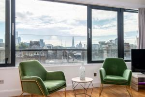 two green chairs in a room with a view of the city at Mulberry South Penthouse by City Living London in London