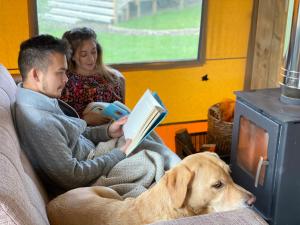 a man and woman sitting on a couch reading a book with a dog at Hencote Vineyard Glamping Village in Shrewsbury