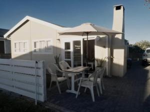 a table and chairs with an umbrella in front of a house at Ons Strandhuisie N5 in Pearly Beach in Pearly Beach