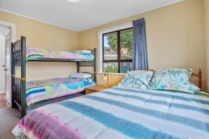 a bedroom with two bunk beds and a window at Kiwiana Bach - Waihi Beach Holiday Home in Waihi Beach