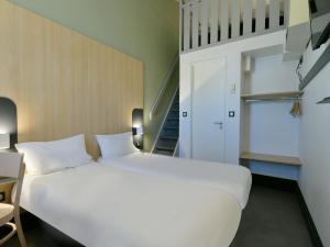 Cama blanca grande en habitación con escalera en B&B HOTEL Le Mans Nord 2, en Saint-Saturnin