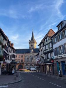eine Stadtstraße mit einer Kirche mit einem Uhrturm in der Unterkunft La Colonne in Obernai