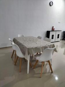 einen Esstisch mit weißen Stühlen, einem Tisch und einer Uhr in der Unterkunft Wipah Guest House in Kampung Lundang, Kota Bharu in Kota Bharu