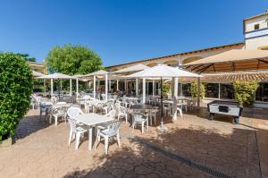 un patio con mesas, sillas blancas y sombrillas en Mariner Club, en Puerto de Alcudia