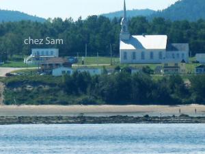 a church sitting on top of a beach next to the water at Auberge du Café chez Sam in Baie-Sainte-Catherine